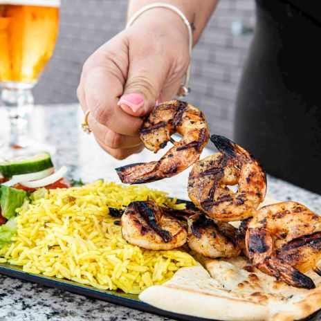 a hand holding shrimp over a plate of rice and salad