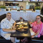 a man and woman sitting at a table with food and drinks